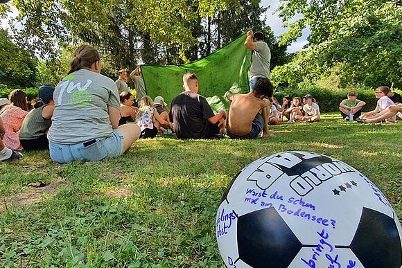 junge Menschen auf einer grünen Wiese im Vordergrund ein Fußball beschrieben