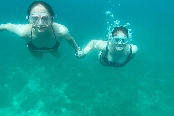 zwei junge Menschen unter Wasser halten sich an den Händen mit Taucherbrillen