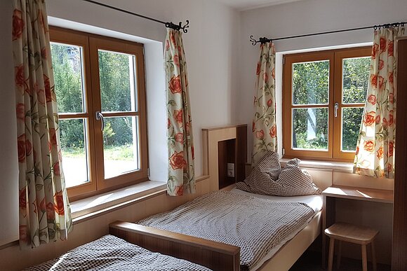 ein sonniges Gästezimmer mit gemusterten Vorhängen und zwei Betten